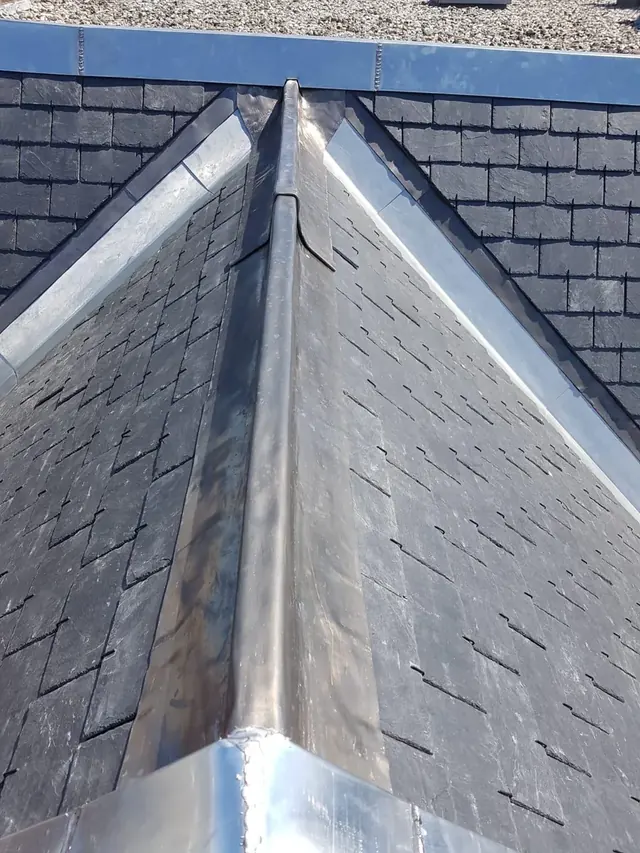 Nok van een leien dak — Metalen nokafwerking boven twee aansluitende leien dakvlakken.